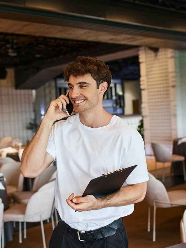 smiling-event-organizer-with-clipboard-talking-on-smartphone-near-festive-tables-in-banquet-hall.jpg